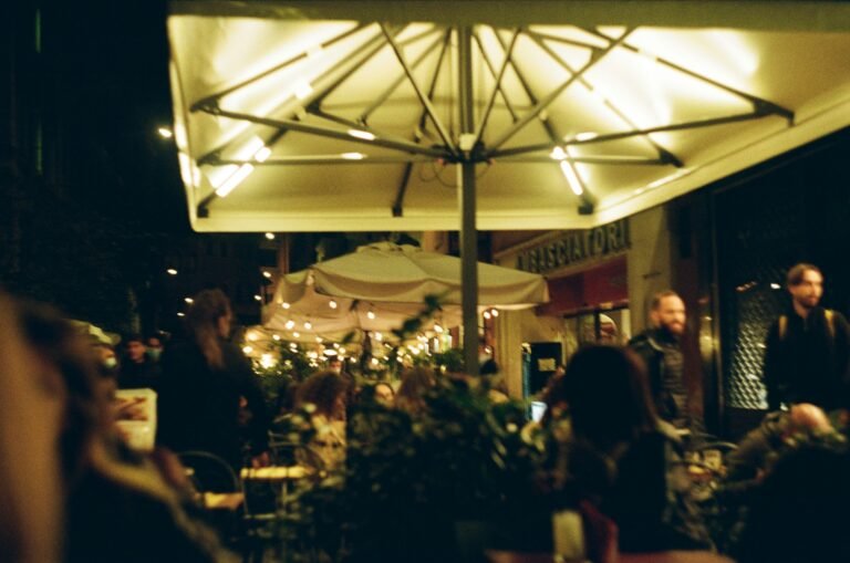 Outdoor restaurant terrace in Bologna at night with warm lights, umbrellas, and people enjoying dinner.