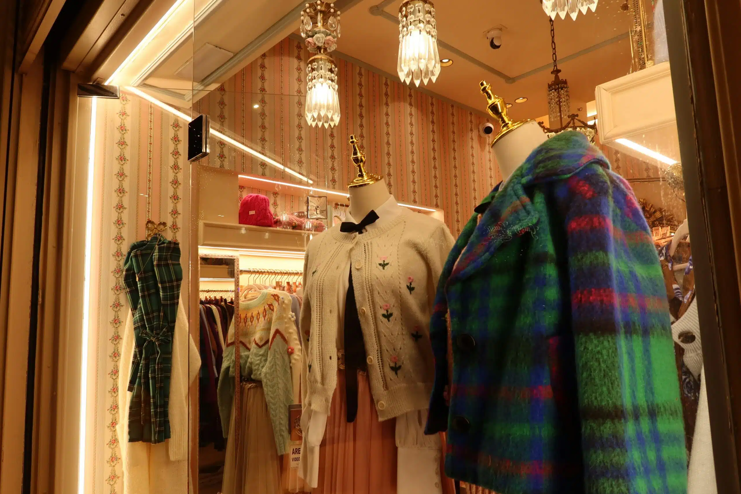 A clothing boutique window with coats and jackets on display beneath hanging chandeliers