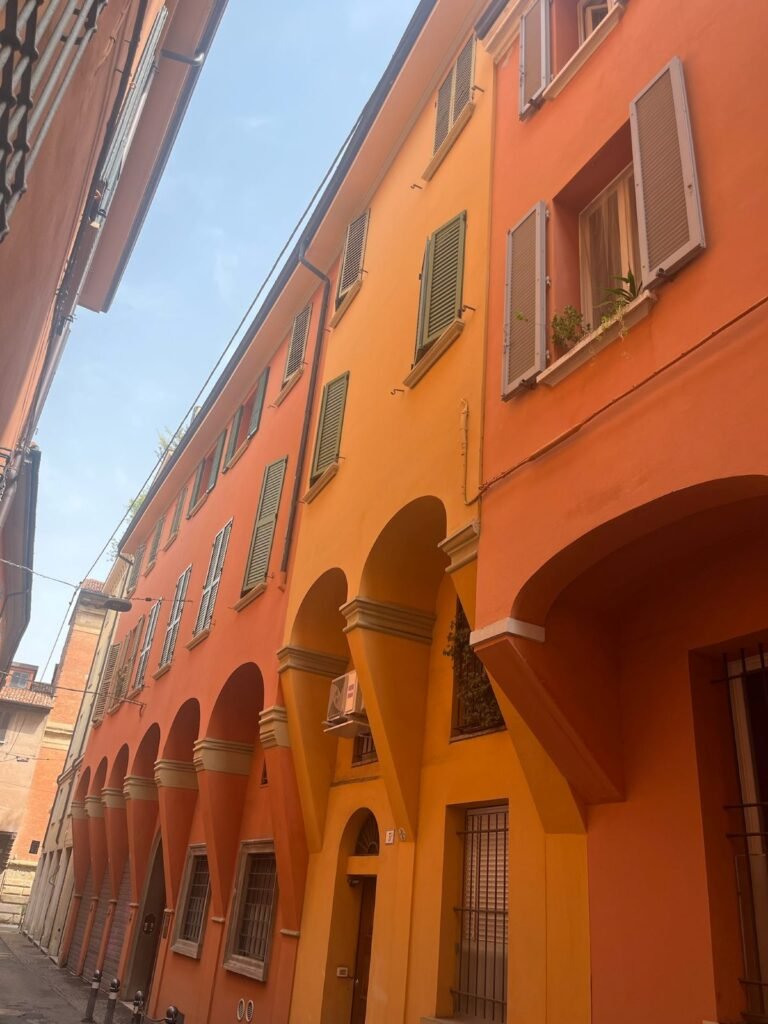 Ochre porticoes with green shutters on a narrow street in central Bologna