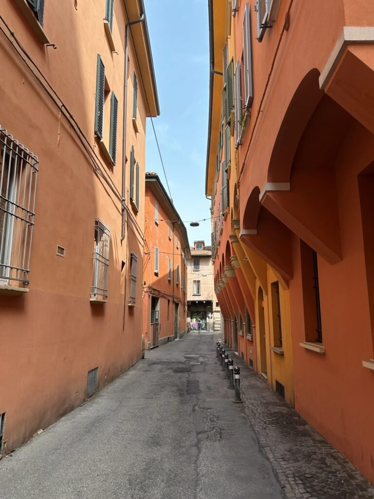 A quiet residential side street in central Bologna, lined with shuttered ochre facades