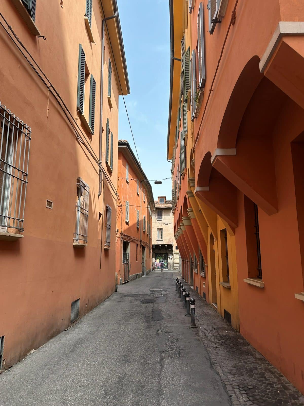 A quiet residential side street in central Bologna, lined with shuttered ochre facades