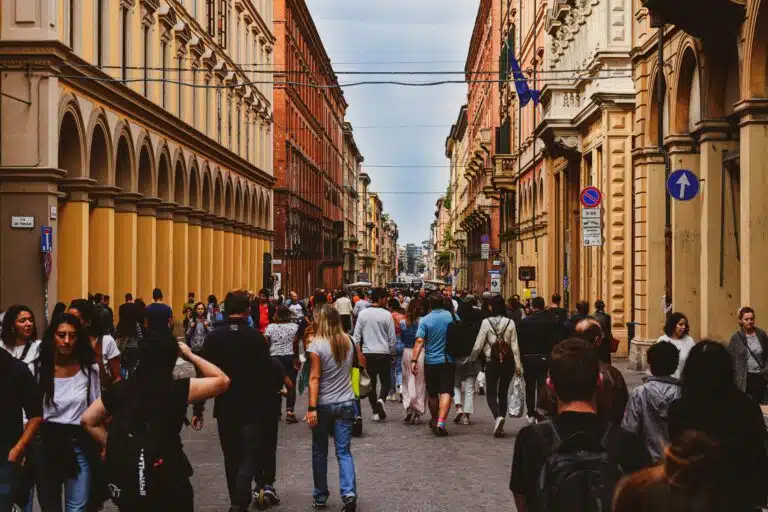 Pedestrians walking along a busy street lined with arcaded buildings in central Bologna